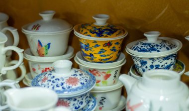 Renkli çiçek ve ejderha desenli çeşitli porselen çay fincanları ve kaseler, geleneksel Çin tarzı seramik sofra takımı olan bir dolaba istiflenmiş..