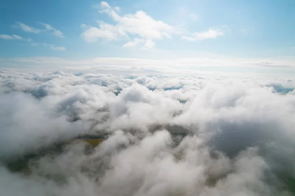 Cumulus clouds, aerial background. Aerial shot with top view of white fluffy clouds gathering. In between the clouds the ground is visible here and there.