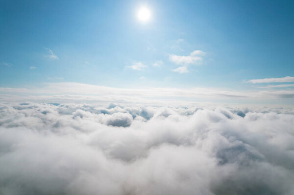 Aerial shot of white fluffy clouds and some blue sky in the distance while flying above the clouds. Aerial background. Beautiful cumulus clouds captured by a drone.