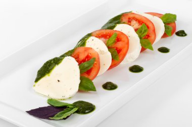 Domates ve mozzarella peyniri dilimleri bir pl fesleğen yaprakları ile süslenmiş