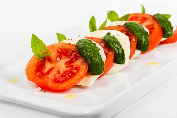 Tomat och mozzarella segment dekorerad med basilikablad på en pl — Stockfoto