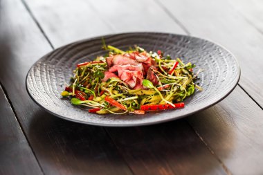 Pastırma taze kırmızı biber, Brüksel lahanası, susam ve zeytinyağı siyah bir plaka üzerinde otantik salatası. Sabah atmosferik aydınlatma, moda trendy spot yumuşak odak. Tasarım yaratıcı menüsü için hazırlık.