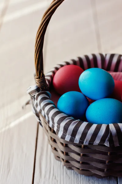 Ovos de Páscoa multicoloridos em cesta de vime no fundo de madeira branco — Fotografia de Stock