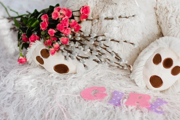 Un hermoso oso de juguete suave se sienta en la cama con flores — Foto de Stock