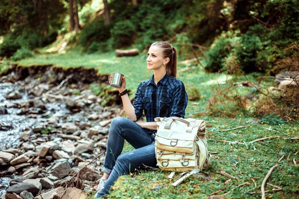 Μικρά τουριστικά κορίτσι κάθεται στην όχθη ενός ποταμού βουνό και να βλέπουν ένα όμορφο τοπίο. Πεζοπορία γυναίκα με χαλαρωτική σακίδιο — Φωτογραφία Αρχείου