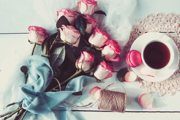 Egy szép csokor Rózsa, tea Cup, a bajba jutott fehér fa asztal macaroons. vintage stílusú — Stock Fotó