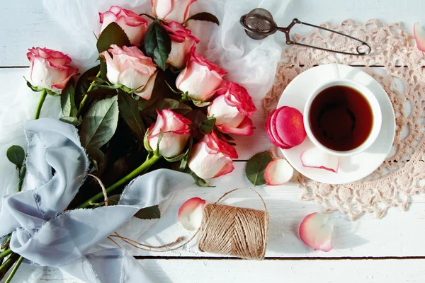 Ein schöner Strauß Rosen, Teetasse, mit Makronen auf einem bedrängten weißen Holztisch. Jahrgangsstil — Stockfoto