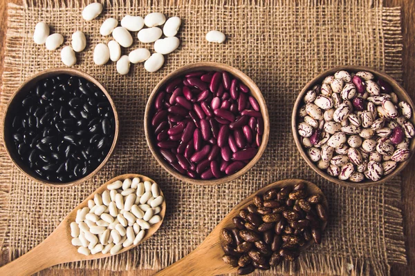 Beautiful multi-colored beans in ceramic bowls on a background of burlap — Stock Photo, Image