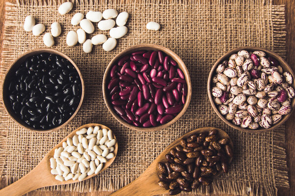 Beautiful multi-colored beans in ceramic bowls on a background of burlap