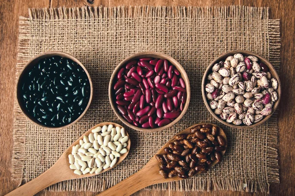 Beautiful multi-colored beans in ceramic bowls on a background of burlap — Stock Photo, Image