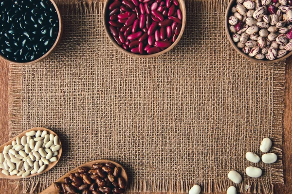 Beautiful multi-colored beans in ceramic bowls on a background of burlap — Stock Photo, Image