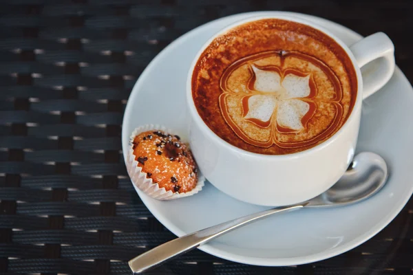 Beautiful white Cup of cappuccino with flower pattern on the foam and cupcake — Stock Photo, Image