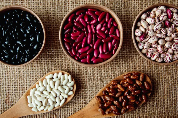 Beautiful multi-colored beans in ceramic bowls on a background of burlap — Stock Photo, Image