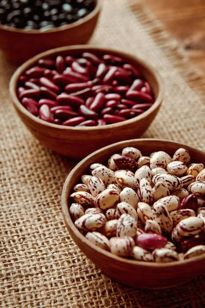 Beautiful multi-colored beans in ceramic bowls on a background of burlap — Stock Photo, Image