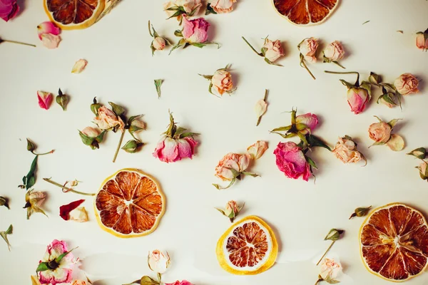 Beau fond avec des roses et des fleurs séchées tranches rondes de citron séchées posées sur un fond blanc — Photo