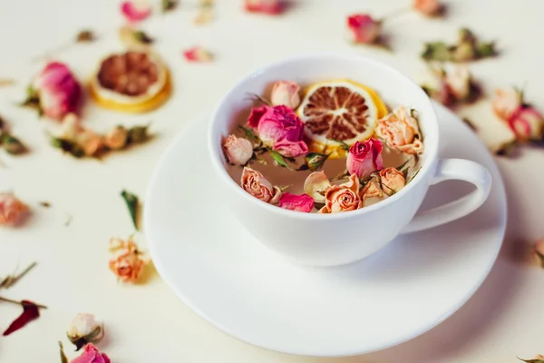 Kräutertee in weißer Tasse und Untertasse mit Rosen und getrockneten Blumen getrocknete runde Zitronenscheiben auf weißem Hintergrund — Stockfoto