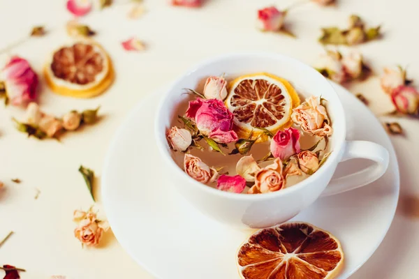 Kräutertee in weißer Tasse und Untertasse mit Rosen und getrockneten Blumen getrocknete runde Zitronenscheiben auf weißem Hintergrund — Stockfoto