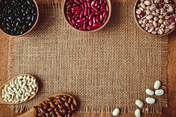 Beautiful multi-colored beans in ceramic bowls on a background of burlap — Stock Photo, Image