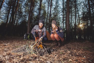 Couple of hikers starting a fire in the wood clipart
