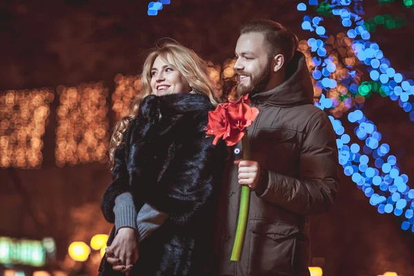 Amando jovem casal andando ao ar livre no inverno. Menina segurando uma flor — Fotografia de Stock
