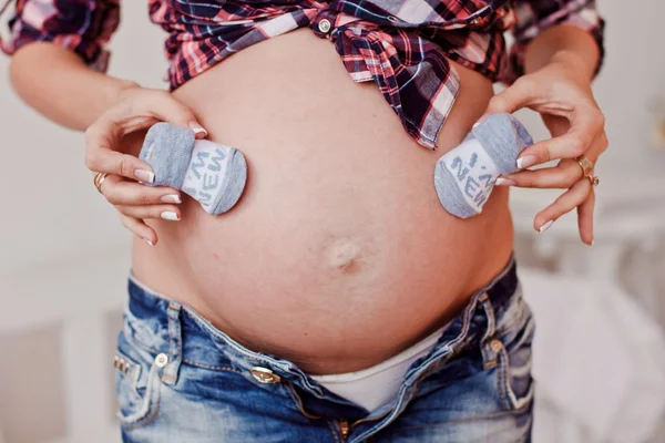 Kleine schoenen voor de ongeboren baby in de buik van een zwangere vrouw — Stockfoto