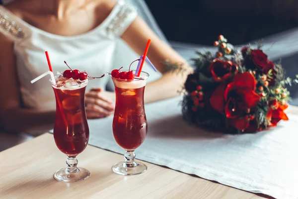 Beautiful red cocktail with cherries and wedding rings, behind the bride with a wedding bouquet of red roses — Stock Photo, Image