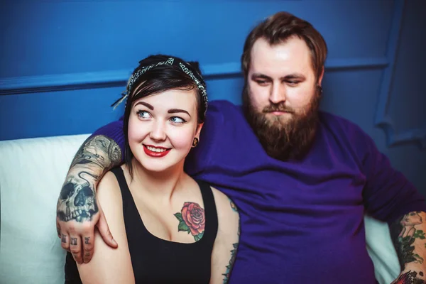 Jeune couple amoureux de tatouages étreignant et tenant la main assis sur le canapé — Photo