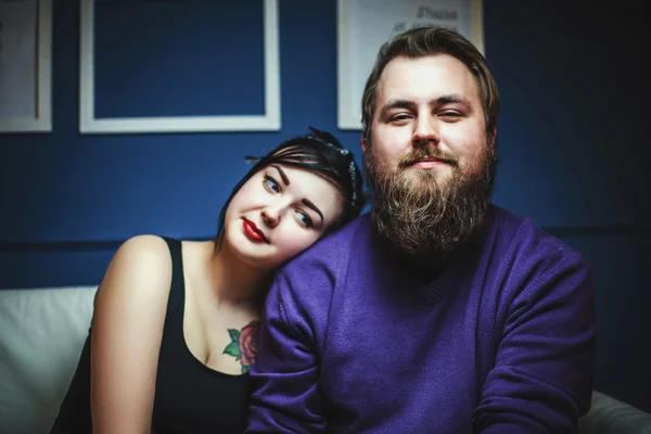 Young couple in love with tattoos hugging and holding hands sitting on sofa — Stock Photo, Image