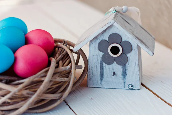 Cor Ovos de Páscoa no ninho no fundo de madeira branco com casa de pássaros — Fotografia de Stock
