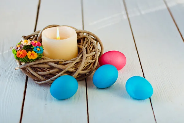 Fundo de Páscoa com vela em um ninho de galhos e ovos coloridos no fundo de madeira branca — Fotografia de Stock