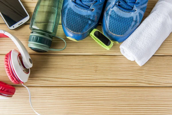 Sport shoes with bottle of water and headphones on wooden background