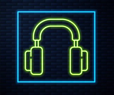 Parlayan neon hattı kulaklık simgesi tuğla duvar arkasında izole edilmiş. Kulaklıklar. Müzik, hizmet, iletişim ve operatör konsepti. Vektör.