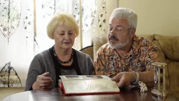 Retired couple looking at an album indoor — Stock Video