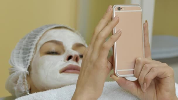 Mujer con máscara facial Navegación por Internet en pantalla táctil Teléfono inteligente en el salón de spa — Vídeo de stock