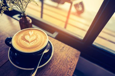 Latte kahve sanatının ahşap masadaki siyah fincanda görüntüsü..