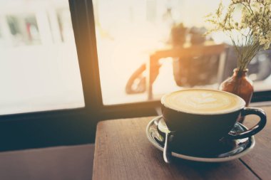 Latte kahve sanatının ahşap masadaki siyah fincanda görüntüsü..