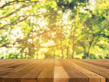 Ahşap tablo ve arkaplan kullanımı için güneş ve güneş ışığı ile yeşil ağaç bokeh soyut bulanık görüntü.