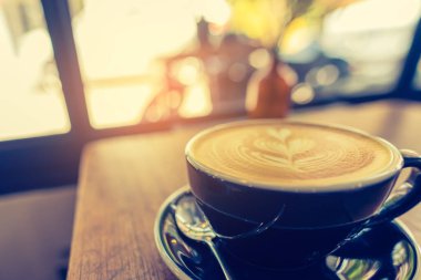 Latte kahve sanatının ahşap masadaki siyah fincanda görüntüsü..