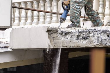 İşçiler binanın dışındaki beton tavanı delip geçiyorlar. Yüksek etkili bir matkapla. Aşağıda toz ve çimento kalıntıları var..
