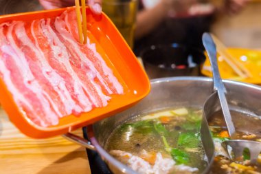 Kore Shabu restoranındaki sıcak kasenin üzerinde dilimlenmiş domuz eti resmi..