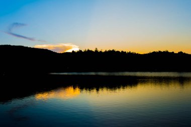 Arka planda ağaç, göl ve günbatımı görüntüsü.