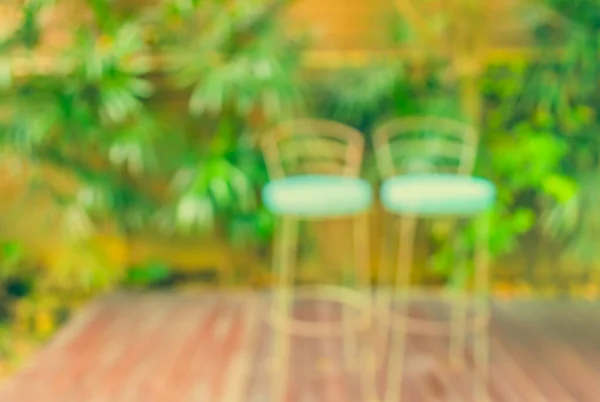 image of Abstract blurred chairs at outdoor coffee hut on day time , with green garden for background usage . (vintage tone)