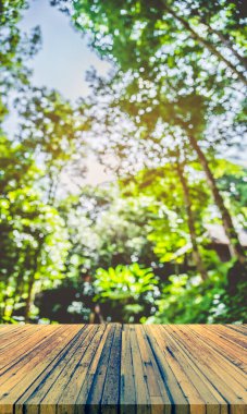 Ahşap masa ve arka plan kullanımı için güneşi olan yeşil ağaç ormanının soyut Bokeh 'inin bulanık görüntüsü. (Klasik ton))