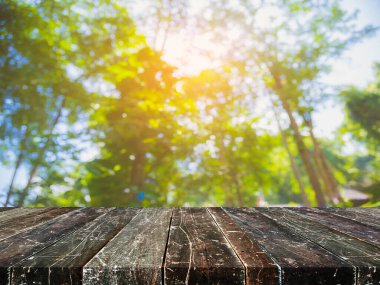 Ahşap masa ve arka plan kullanımı için güneşi olan yeşil ağaç ormanının soyut Bokeh 'inin bulanık görüntüsü. (Klasik ton))