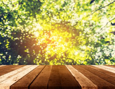 Ahşap tablo ve arkaplan kullanımı için güneş ve güneş ışığı ile yeşil ağaç bokeh soyut bulanık görüntü.