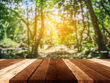 Ahşap masa ve arka plan kullanımı için güneşi olan yeşil ağaç ormanının soyut Bokeh 'inin bulanık görüntüsü. (Klasik ton))