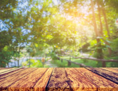 Ahşap masa ve arka plan kullanımı için güneşi olan yeşil ağaç ormanının soyut Bokeh 'inin bulanık görüntüsü. (Klasik ton))