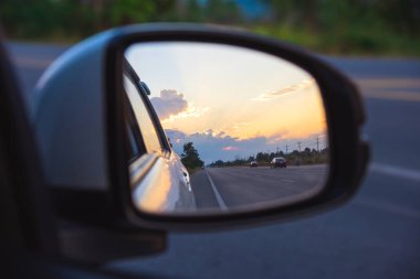 Gün batımında arka planda perspektif yolunu görmek için araba kanadı aynası görüntüsü.