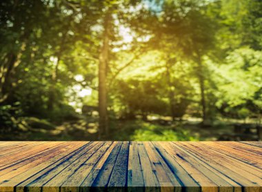 Ahşap masa ve arka plan kullanımı için güneşi olan yeşil ağaç ormanının soyut Bokeh 'inin bulanık görüntüsü. (Klasik ton))