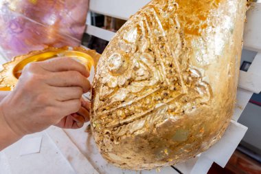 Elin altın çarşaf tutarak Tayland tapınağındaki kutsal altın kaplama heykele yapıştığı görüntüyü kapatın..